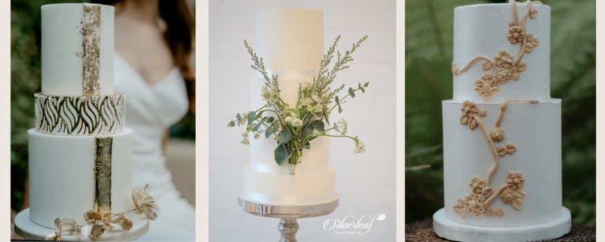 Three bespoke tiered wedding cakes featuring gold leaf accents, fresh green foliage, and sculpted neutral floral vines by Silverleaf Cake Company.