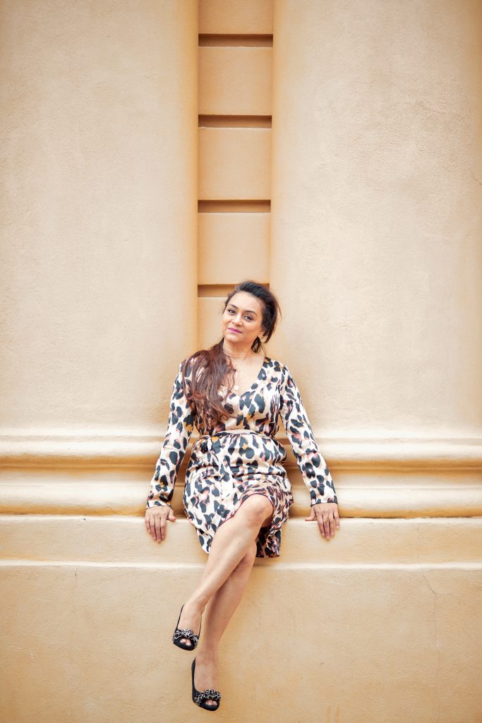 Portrait of a contemporary wedding cake designer in a silk leopard print dress, seated against a cream stone building in London