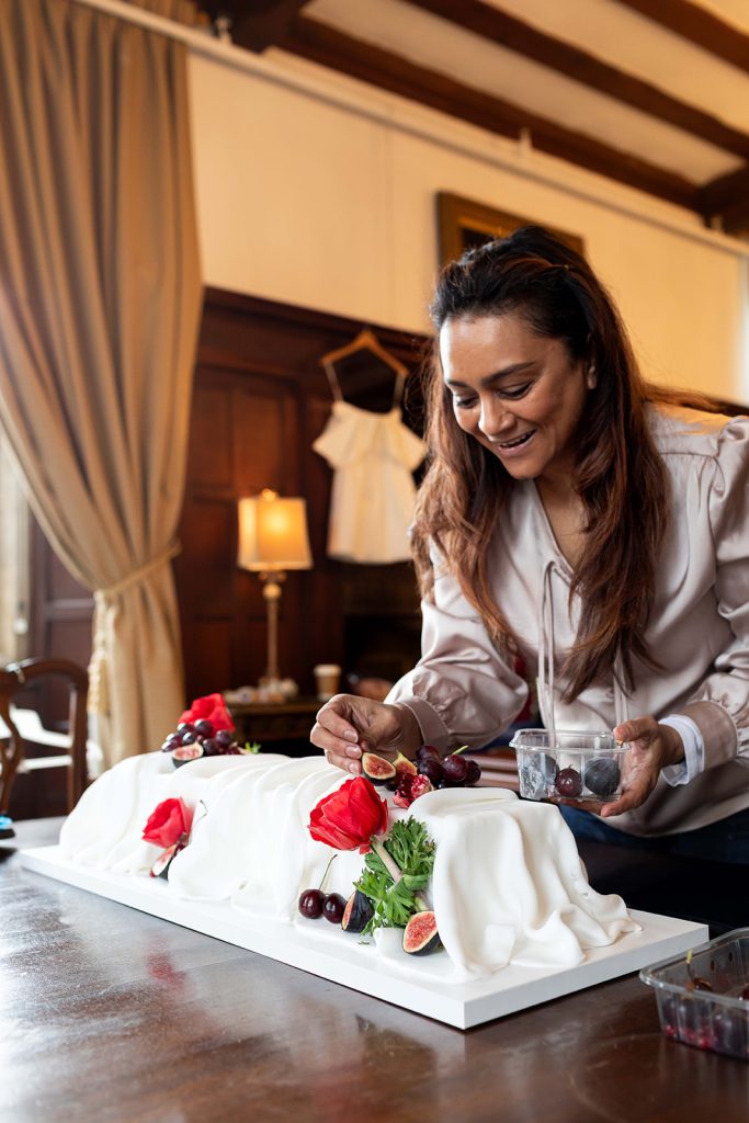 Modern wedding cake artist Northampton Parul decorating long sculptural wedding cake with fruit and sugar flowers