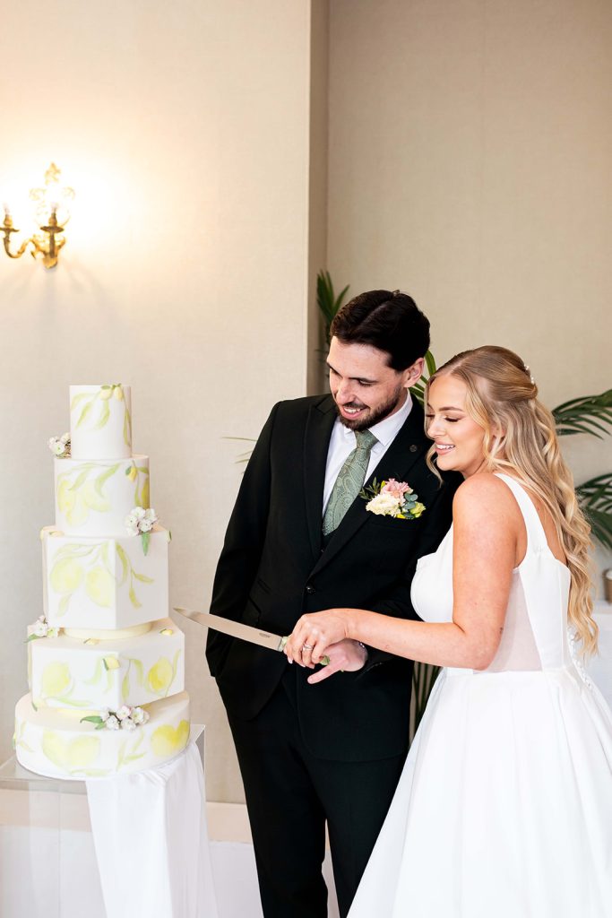 Bride and groom cutting five-tier white wedding cake with hand-painted lemons, 3D lemons and sugarpaste cherry blossoms