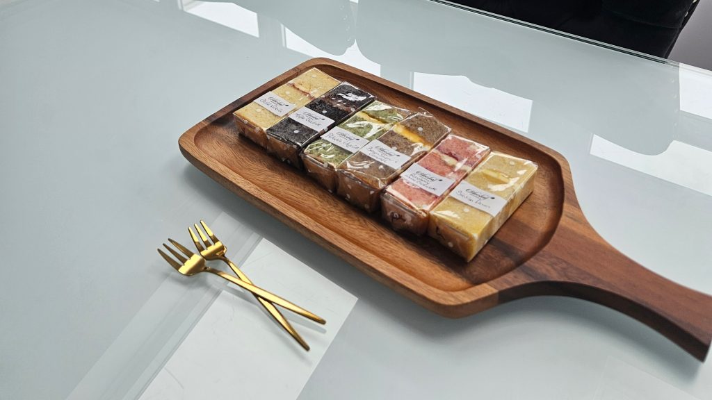 Wedding cake sample slices with labelled flavours on wooden board with gold forks