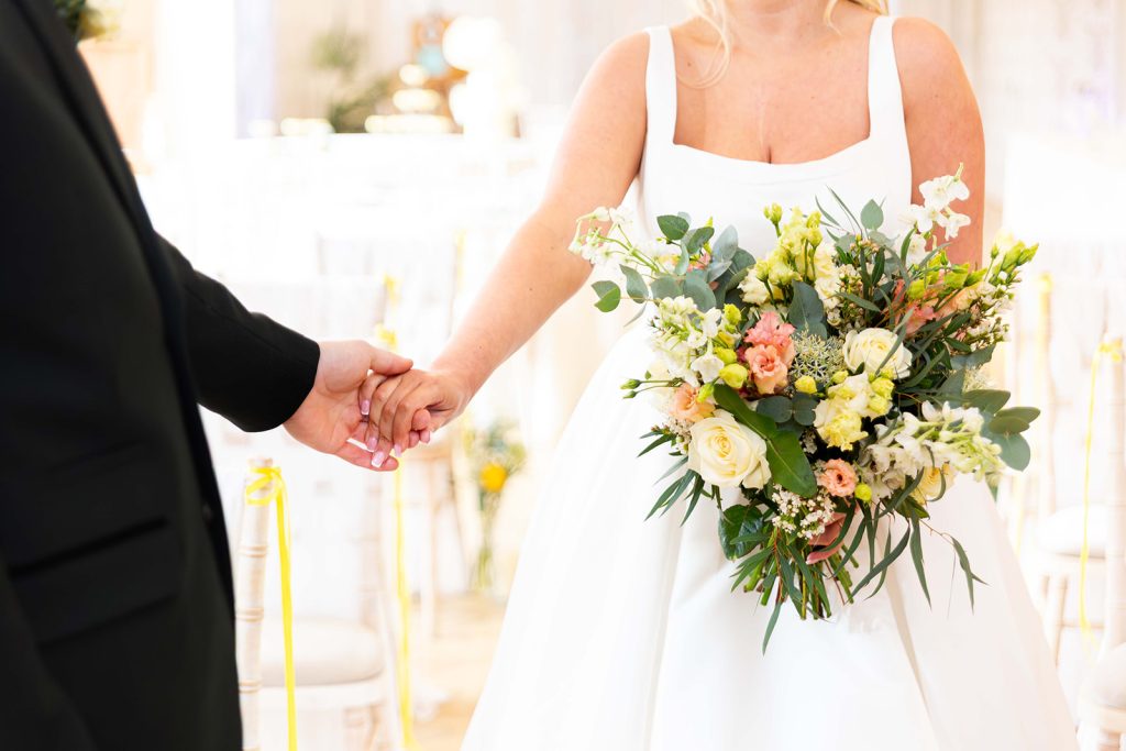 Bride and groom holding hands in wedding attire with lemon coloured bouquet