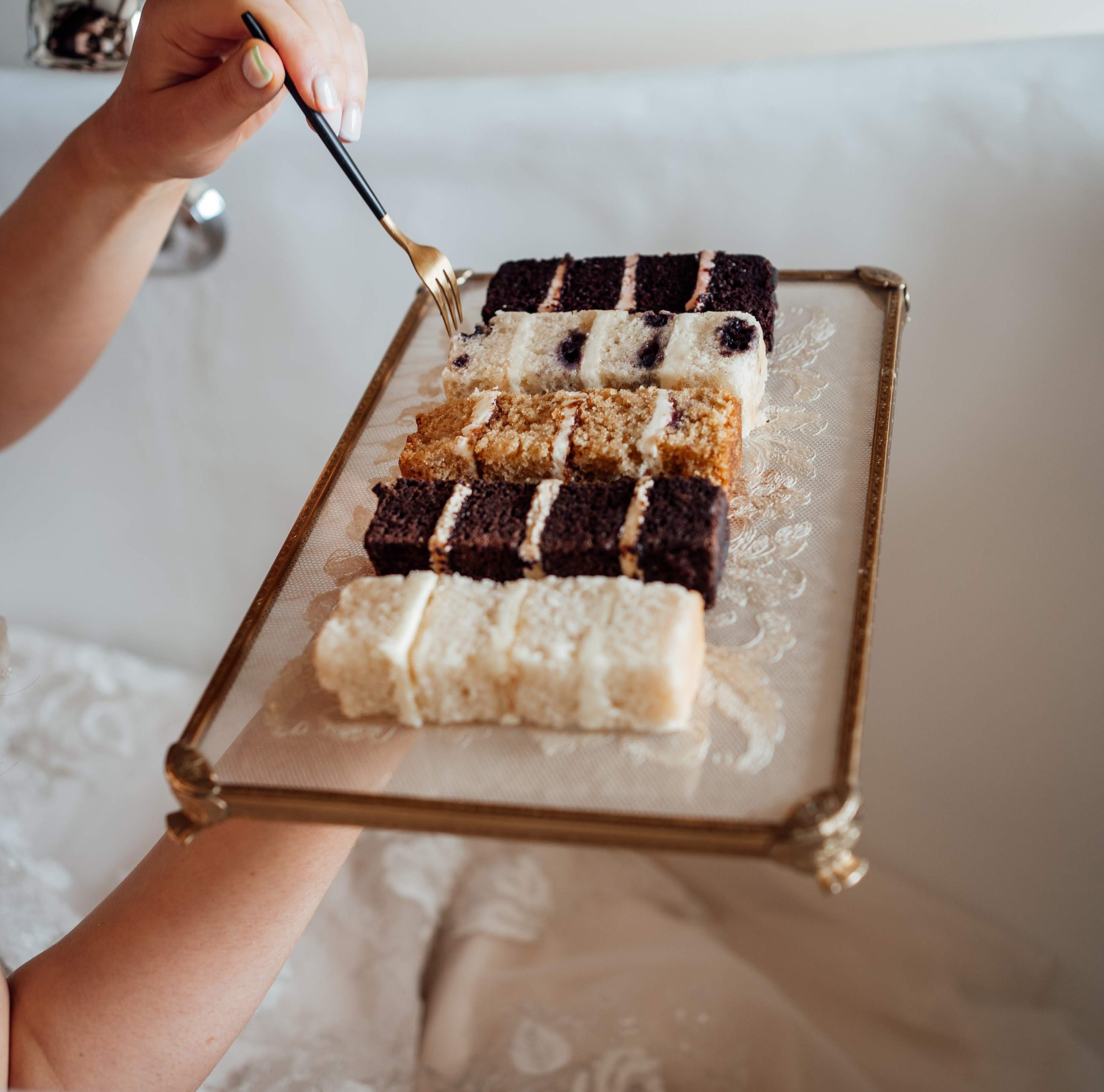 Wedding cake flavours, Bride holding gold fork with wedding cake samples on antique lace tray