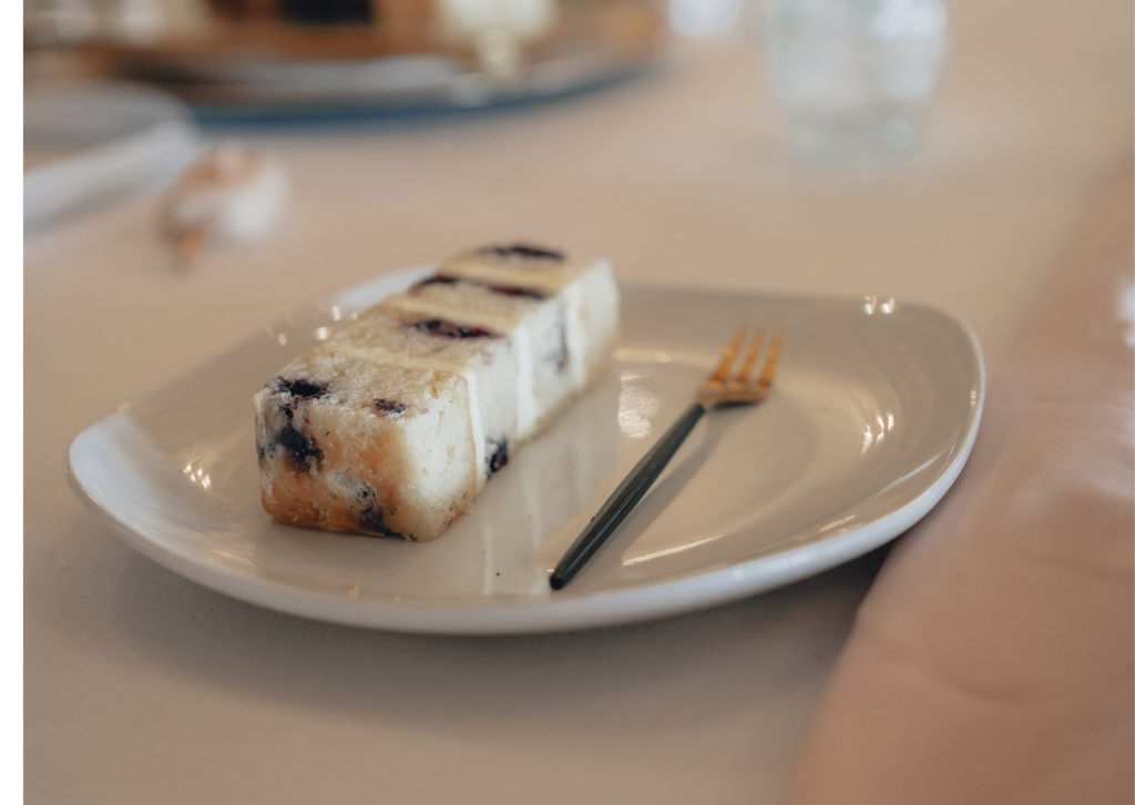 Vegan wedding cake flavours , vegan Blueberry and lemon wedding cake slice on white plate with gold fork