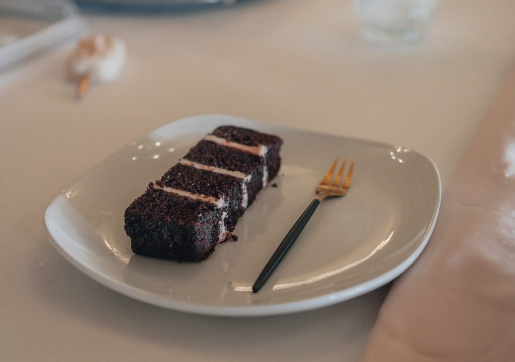 Wedding cake Flavours - Chocolate and raspberry wedding cake slice on white plate with gold fork
