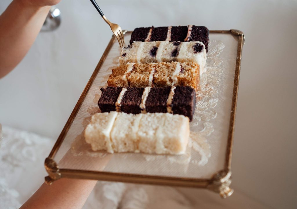 Wedding cake flavours, Bride holding gold fork with wedding cake samples on antique lace tray