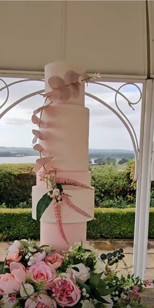 Blush and peach tone 5 tier wedding cake set in an outdoor setting on a floral plinth in a pagoda